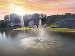 Fountain in a pond with houses and trees in the background during sunset.