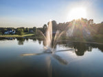 Fountain in a pond with houses and trees in the background