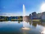 Fountain in a pond with houses and trees in the background