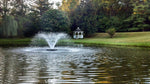 Fountain in a pond with a gazebo in the background, surrounded by trees and greenery.