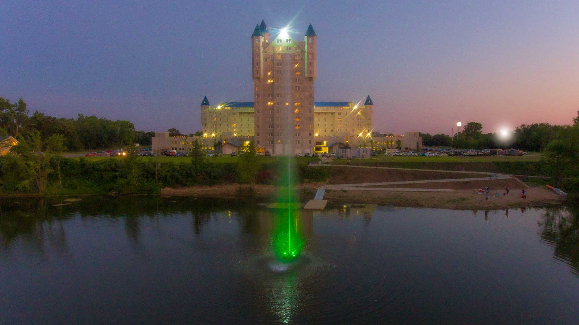 A jet stream fountain shooting water vertically in a pond with a building illuminated in the background.