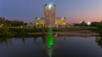 A jet stream fountain shooting water vertically in a pond with a building illuminated in the background.