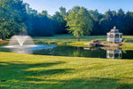 Pond with fountain and gazebo surrounded by trees on a sunny day